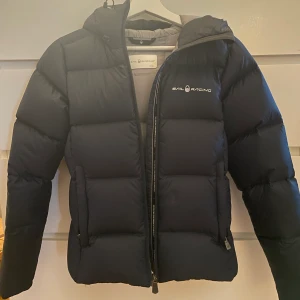Dunjacka Sailracing - Dunjacka från Sailracing i storlek xs, köpt här på Plick men måste tyvärr sälja vidare då den var lite liten på mig. Jättefint skick utan några som helst slitningar. Nypris ca 3800kr. Kan mötas upp men även skickas via post 🫶🏻 