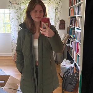 Mörkgrön vinterjacka - En grön vinterjacka, vadderad och mycket bra till vintern. Lite längre och funkar även som skidjacka. Luvan är avtagningsbar och den har tre fickor varav en innerficka :)