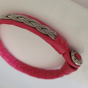 Tenntrådsarmband rosa ca 17 cm - Klassiskt tenntrådsarmband med rosa läder. Fin knapp. Ny, aldrig använd. Storlek ca 17cm, vuxen.