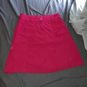 Cappuccini kjol rös strl 36 - En fin Cappuccini wear kjol i strl 36. Den har lite cargo stil eftersom att den har en "sido" ficka på höger sida. Köpt secondhand  men jag har aldirg använt den. Skulle säga att den är i bra skick. Från början av kjolen ner är den 54 cm. GÅR NER TILL KNÄ