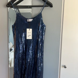 Glittrig klänning  - Säljer en blå glittrig klänning från Linn Ahlborg x NA-KD i storlek 32, stor i storleken. Aldrig använd med lapp kvar. Köpt för kanske 2 år sedan. 
