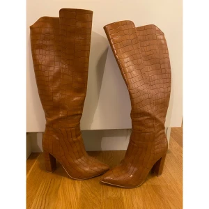 Knähöga bruna stövlar  - Jättefina bruna knähöga stövlar i fakeskinn. Använda ett fåtal gånger så de är i superfint skick. Dock är det en liten slitning på ena skon längst fram på spetsen. Storlek 39. Hämtas hos mig i Göteborg eller skickas mot att köparen betalar frakt. 