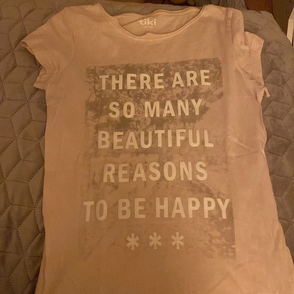 Rosa T-shirt med en text där det står there are so many reasons to be happy . T-shirts.