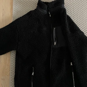 Teddyjacka - Svart teddyjacka. Snyggt oversized och går en bit över rumpan. Kan dras upp högt i halsen. Är storlek small men sitter oversized på mig som vanligtvis är en medium. Köptes i vintras och väldigt sparsamt använd.