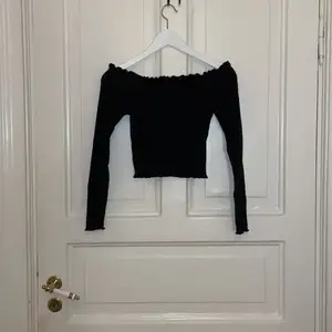 Svart off shoulder tröja från Gina Tricot. Den är tight i modellen och ganska kort. På alla ändar av tröjan finns det små voulanger 🫶🏼💫