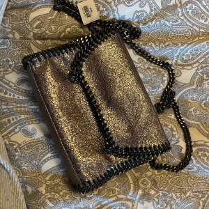 Glittrig väska  - Säljer denna glittriga rosa/lila väska från Ullared. Prislapp kvar då den aldrig är andvänd. Långt kedje band. 