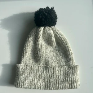 Stickad mössa - Stickad mössa med svart tofs. Knappt använd. 
