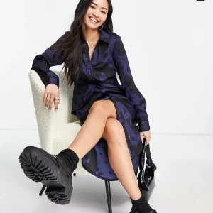 Stradivarius - Blå skjortklänning i satin med snurrad knut  - En jätte fin blå klänning som är perfekt nu till hösten då den är lite längre. Den är aldrig använd, prislappen sitter fortfarande på. Den är i storlek XL men passar definitivt L för den är lite tajtare i modellen. 