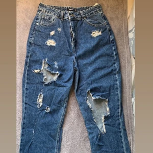 Boyfriend Jeans med Hål  - Boyfriend Jeans med hål på framsidan ifrån BooHoo i storlek 40. Har en liten fläck med färg längst ner på baksidan av ett ben. Använda fåtal gånger. 100kr+frakt (cirka 50kr)