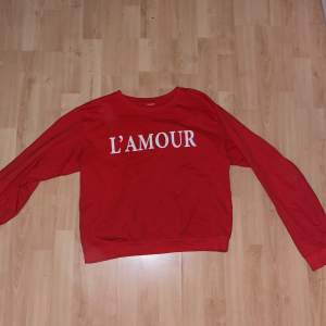 Lindex röda sweatshirt med vit L’amour text. Tunn sweatshirt i röd färg. Klippt lapp i tröjan. 