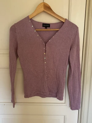 Lila och glittrig kofta - En superfin lila kofta med inslag av silvrigt glitter. Den har även fina detaljer av holografiska paljetter. Knappt använd och i mycket bra skick.