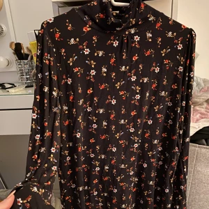 Blus - Svart blus med blommor på från Cubus i storlek S. Hög hals. Ej använd och i superskönt/luftigt material. Säljer för 50kr+frakt
