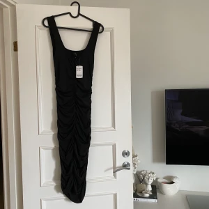 Klänning  - Snygg svart basic klänning. Skrynklad på baksidan och slät på framsidan, för att framhäva kurvor. Aldrig använd, prislapp kvar.
