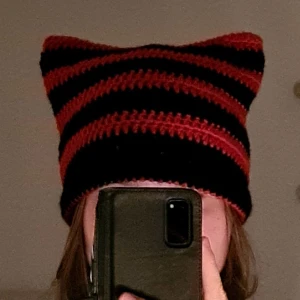 röd/svart cat beanie  - Egenvirkad cat beanie i röd och svart! Passar de flesta och är gjord med 100% akrylgarn. Tveka inte på att höra av dig vid frågor🫶