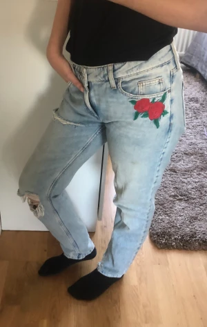 Jeans - Jeans med dekorativa hål och broderad ros. Storlek: XS (relaxed modell) Märke: Köpt från Cubus. Använd men den är i okej skick. 