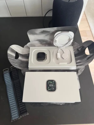 Apple smartklocka med extra armband - Snygg Apple smartklocka i silver med fyrkantig form och stor skärm. Medföljer laddkabel och två armband, ett svart och ett blått. Perfekt för dig som vill ha koll på träning, notiser och hälsa direkt på handleden.