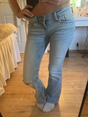 Ljusblå bootcut jeans med slitningar - Säljer ett par ljusblå bootcut jeans med slitningar på knät och låret. Jeansen har låg midja och lätt utsvängda ben. Materialet är denim i bomull med en mjuk tvättad känsla. Jeansen är från Gina orginalt men tycker att de är för korta på mig. Använda ca 5 gånger