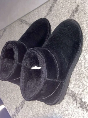 Svarta uggs - Svarta uggs från Nelly med kort skaft och mjukt, fluffigt foder på insidan. Utsidan är i mockaimitation och sulan är rejäl. Perfekta för att hålla värmen under kyliga dagar.