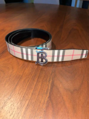 Äkta Burberry bälte - Snyggt Burberry bälte i beige med klassiskt rutigt mönster i brunt, vitt och röt. Det är äkta och verifierat av vesitire collectives. 