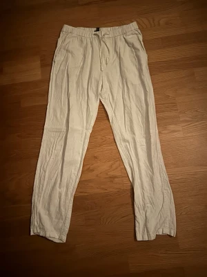 Vita linnebyxor från H&M - Säljer ett par vita linnebyxor från H&M med relaxed fit och dragsko i midjan. Byxorna har raka ben och elastisk midja för extra komfort. Perfekta för en chill och avslappnad stil under varmare dagar.