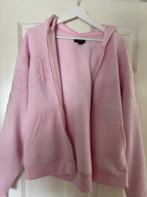 Ljusrosa hoodie från boohooMAN - Säljer en ljusrosa hoodie från boohooMAN i storlek M. Hoodien har dragkedja, två stora fickor framtill och broderade detaljer på bröstet och ärmen. Tillverkad i mjukt sweatshirtmaterial och har en klassisk huva. Perfekt för en chill och avslappnad stil.