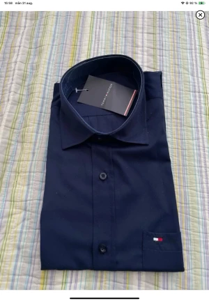 Mörkblå skjorta från Tommy Hilfiger - Snygg mörkblå skjorta från Tommy Hilfiger med klassisk krage och knappar framtill. Liten logga broderad på bröstfickan. Perfekt till både jeans och chinos för en clean look.