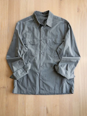 Olivgrön overshirt med fickor - Stilren olivgrön overshirt i bomull med två bröstfickor med knappstängning och sidofickor. Klassisk krage och knäppning framtill. Perfekt lager på lager-plagg för en avslappnad look.