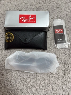 Svarta Ray-Ban solglasögon - Snygga svarta solglasögon från Ray-Ban med klassisk Wayfarer-form. Kommer med originalfodral, putsduk och box. Glasen är mörka och bågarna är mattsvarta med Ray-Ban-logga på sidorna. Perfekta för att höja din stil i solen.