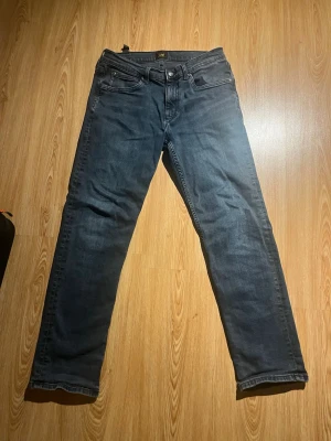 Mörkblå raka jeans Lee - Snygga mörkblå jeans från Lee med klassisk femficksdesign och raka ben. Jeansen har en diskret tvättad look och Lee-logga på bakfickan. Perfekta för en avslappnad och stilren outfit.