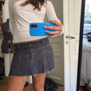 Mörkblå jeanskjol - Säljer en supersnygg mörkblå kort jeanskjol med rå, fransig kant och gula sömmar. Kjolen har fickor fram och bak, dragkedja och en snygg detalj med dubbla knappar framtill. Kjolen är avklippt samt snitt på båda sidorna för att få ett annan typ av fall men det är inget märkbart när den väl är på. Står att kjolen är i XL men skulle nog passa mer en M/L