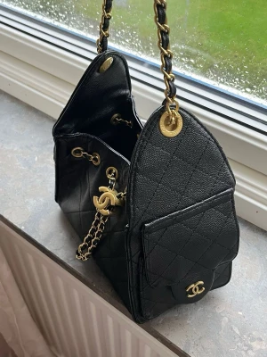 Svart  handväska med guldkedja - Snygg svart handväska från  i quiltat läder med guldfärgade detaljer och kedja. Väskan har ett klassiskt CC-spänne framtill, ytterfack och axelrem i kedja och läder. Perfekt för dig som gillar lyxig och tidlös design.