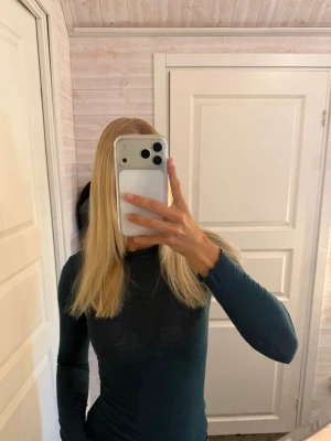 Mörkgrön långärmad topp - En enkel och stilren mörkgrön långärmad topp med rund hals. Toppen har en tight passform och är tillverkad i ett mjukt material som känns skönt mot huden. Perfekt att matcha med jeans eller kjol för en clean look.