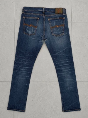 Nudie Jeans 31/34 - Snygga blå jeans från Nudie Jeans med smal passform och klassisk femficksdesign. Jeansen har slitningar och kontrastsömmar samt Nudie Jeans signaturbroderi på bakfickorna. Tillverkade i denim med en cool tvättad look.