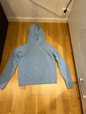 Ljusblå hoodie med magficka - En stilren ljusblå hoodie med huva och stor magficka framtill. Hoodien har långa ärmar och ribbade muddar vid ärmslut och nederkant. Perfekt för en avslappnad och chill look.