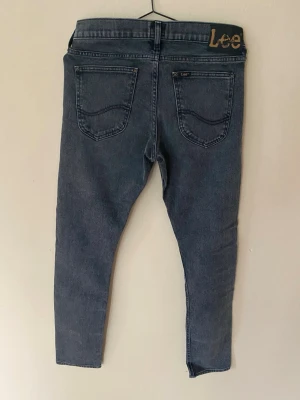 Mörkgrå slim fit jeans från Lee - Snygga mörkgrå skinny jeans från Lee med klassisk femficksdesign och hög midja. Jeansen har en smal passform och är tillverkade i stretchigt denimtyg för extra komfort. Perfekta för en avslappnad och trendig look. Storlek W29 L32 se sista bild! Topskick 
