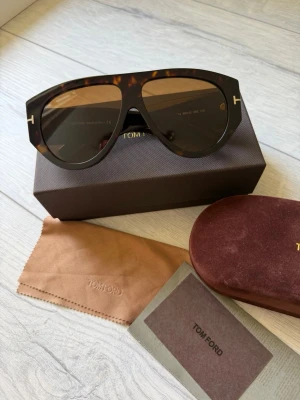Tom Ford bruna solglasögon - Snygga solglasögon från Tom Ford i brunsköldpaddsfärgad plast med bred båge och ikoniska T-detaljer i guld på sidorna. Medföljer originalfodral, putsduk och låda. Perfekt accessoar för att lyfta din stil.