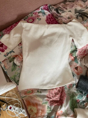 Vit ribbad off shoulder topp - Säljer en vit ribbad topp med off shoulder-modell och korta ärmar. Tyget är stretchigt och har en mjuk känsla, perfekt för en trendig och enkel look. Passar till både jeans och kjol för en snygg outfit. En liten deffekt under ena armen men ingt som syns när man har på sig den.🤗