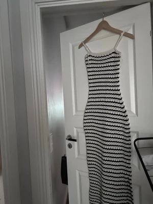 Randig långklänning från Gina Tricot - Säljer en lång, stickad klänning från Gina Tricot i storlek S. Klänningen har smala axelband och är vit med svarta ränder. Materialet är stickat och ger en cool, somrig vibe. Perfekt för dig som gillar en avslappnad men ändå trendig look.