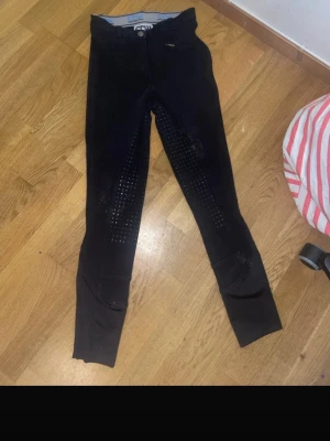 Svarta ridleggings med silikon - Säljer ett par svarta ridleggings med hög midja och silikon på insidan av benen för extra grepp. De har en smal passform och stretchigt material som ger bra rörelsefrihet. Perfekta för dig som vill ha bekväma och funktionella leggings till ridning.