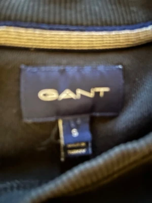 Svart hoodie från GANT, storlek S - Svart hoodie från GANT i storlek S. Klassisk modell med ribbade muddar vid ärmslut och nederkant. Perfekt för en avslappnad och stilren look. Materialet känns mjukt och bekvämt mot o huden Må se liten ut men lita på mig den är inte de. .