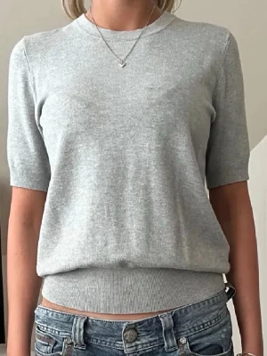 Ljusgrå topp från Zara - Säljer en ljusgrå topp från Zara med rund halsringning och korta ärmar. Toppen har en ribbad kant nedtill och är gjord i mjukt material som känns skönt mot huden. Enkel och stilren modell som passar till det mesta.