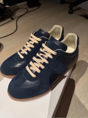 Maison margiela Gats  - Snygga marinblå sneakers i mocka och läder med beige snören och vit insida. Skorna har en klassisk låg siluett och gummisula som ger en retrovibe. Perfekta för dig som gillar stilrena och tidlösa sneakers.allt Og följer med!