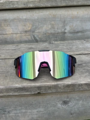 Pastellrosa och svart sportglasögon spegelglasade solglasögon - Säljer ett par riktigt snygga sportiga solglasögon med spegelglas i regnbågsfärger. Glasögonen har en kantig, futuristisk form och svarta bågar. Perfekta för dig som vill sticka ut och samtidigt skydda ögonen mot solen.