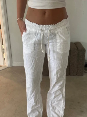 Roxy Vita linnebyxor  - Säljer ett par vita linnebyxor med avslappnad passform och resår i midjan. Byxorna har dragsko och två stora fickor framtill. Perfekta för en chill och stilren look under varma dagar. Säljer då dem är försmå💕(inte mina bilder)