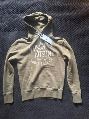 Maison Kitsuné Hoodie - Helt ny Maison Kitsuné Hoodie! Tvär fett khaki färg, alltså Militär grön med lite brun blandning. Storlek S sitter Slim. Butikspris 2300kr helt slutsålda! Skriv vid funderingar😝
