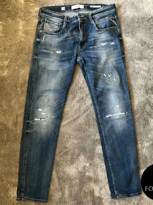 Blå slitna skinny jeans herr - Snygga blå skinny jeans med slitningar och distressed detaljer på både fram- och baksida. Klassisk femficksmodell med dragkedja och knapp. Jeansen har en tvättad look och smal passform som ger en modern vibe. Har några difekter i skrevet, men inget som syns när de sitter på. Hör av er vid frågor.