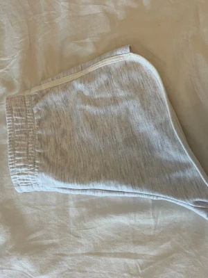 Ljusgrå sportiga shorts med resår - Snygga ljusgrå shorts med elastisk midja och vit kant längs sidorna. Perfekta för en avslappnad stil eller träning. Tillverkade i mjukt bomullsmaterial.