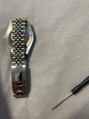  Datejust silverfärgad klocka - Stilren  Datejust herrklocka i silver med klassisk jubilee-länk och räfflad bezel. Urtavlan är mörkgrå med tydliga index och datumfönster med förstoringsglas. Klockan har en robust känsla och passar perfekt till dig som gillar exklusiva accessoarer. OBS helt ny köpt för att sälja vidare. Du får me allt på bilderna, du kan justera den hur du vill.
