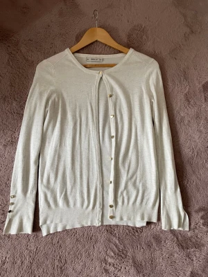 Vit kofta från ZARA Knit - Snygg och enkel vit kofta från ZARA Knit med rund halsringning och guldfärgade knappar framtill samt vid ärmsluten. Lätt och tunnstickad modell som passar perfekt till lager på lager. Klassisk och stilren design som funkar till det mesta.