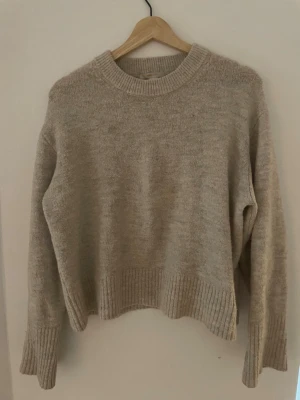 Beige stickad tröja med rund hals - Mysig beige stickad tröja med rund halsringning och ribbade muddar vid ärmslut och nederkant. Tröjan har en avslappnad passform och är perfekt för lager-på-lager-stil. Passar dig som gillar en enkel och stilren look.